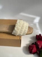 صندل زنانه تزیینی با نخ، مروارید و صدف روی جعبه مقوایی با پس‌زمینه گل رز قرمز